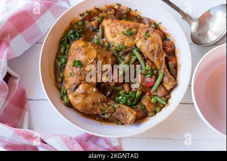 Gedünstete Hähnchenschenkel mit Gemüse, Kartoffeln und Hülsenfrüchten in einer Schüssel auf weißem Hintergrund Stockfoto