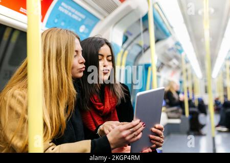 Großbritannien, London, zwei junge Frauen im Untergrund, die ein digitales Tablet benutzen Stockfoto