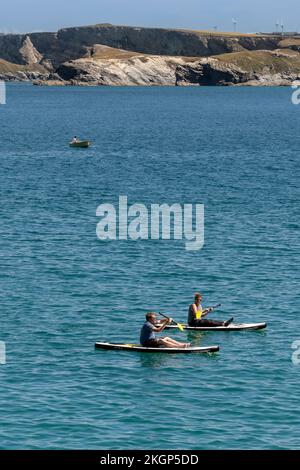 Zwei Urlauber sitzen auf Stand Up Paddleboards in Newquay Bay in Cornwall in England im Vereinigten Königreich. Stockfoto