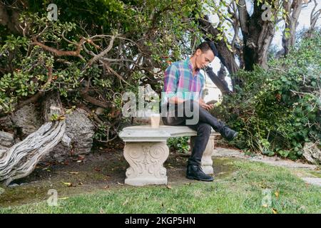 Mann sitzt auf einer Bank und benutzt Smartphone im Park Stockfoto