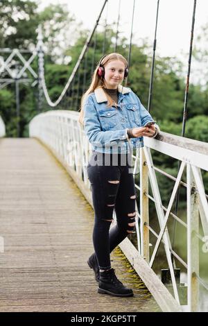 Teenager, die ein Smartphone benutzt und Musik auf einer Brücke hört Stockfoto