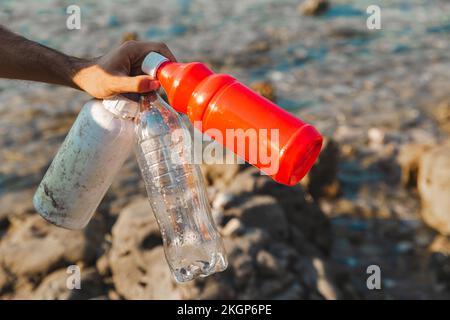 Hand eines Mannes, der leere Plastikflaschen am Strand hält Stockfoto