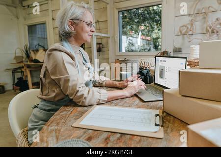 Handwerkerin mit Laptop auf Werkbank in der Werkstatt Stockfoto