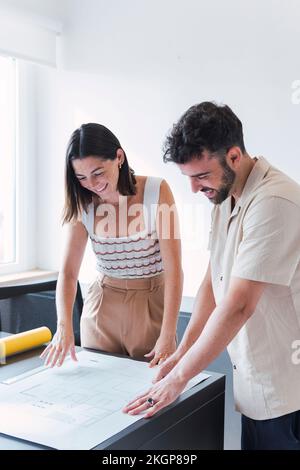 Glückliche Geschäftskollegen, die im Büro über den Blueprint diskutieren Stockfoto