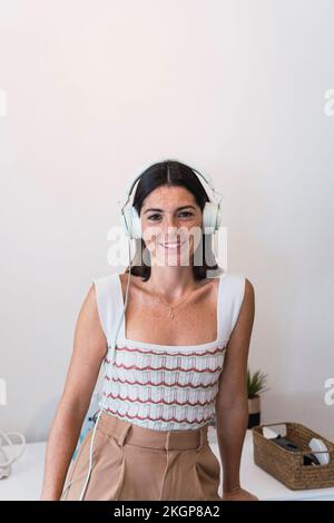 Glückliche junge Geschäftsfrau mit Kopfhörern, die im Büro Musik hört Stockfoto