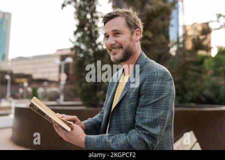 Glücklicher Mann mit Buch auf der Bank Stockfoto