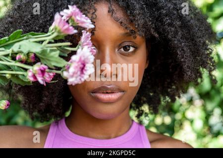 Junge Frau, die violette Blumen vor dem Auge hält Stockfoto