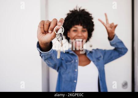 Fröhliche Frau, die Hausschlüssel und Friedenszeichen vor der Tür zeigt Stockfoto