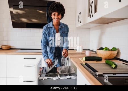 Glückliche junge Frau, die Plastikflaschen zu Hause in der Küche recycelt Stockfoto