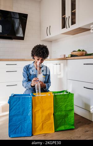 Lächelnde Frau recycelt Plastikflaschen in Mehrwegbeuteln zu Hause Stockfoto