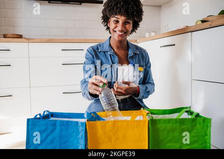 Glückliche Frau, die Plastikflaschen zu Hause in Mehrwegbeuteln recycelt Stockfoto