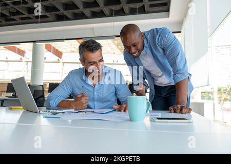 Lächelnde Geschäftsleute, die sich am Schreibtisch über Dokumente unterhalten Stockfoto