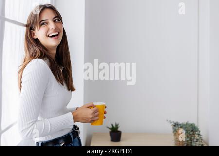 Eine schöne Frau, die zu Hause lacht und eine Kaffeetasse hält Stockfoto