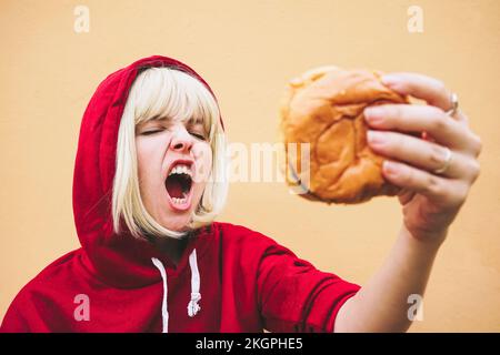 Eine Frau mit geschlossenen Augen, die Hamburger vor der Pfirsichwand hält Stockfoto