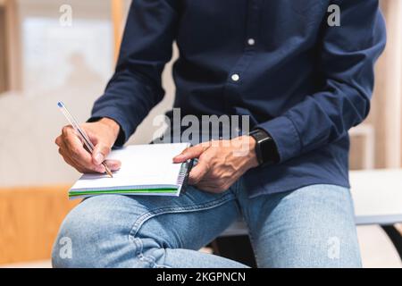 Hand eines Geschäftsmannes, der auf dem Schreibtisch in ein Tagebuch schreibt Stockfoto