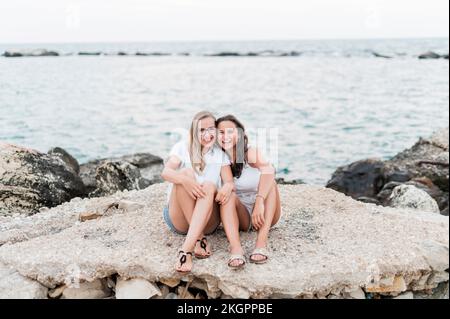 Fröhliche Freunde, die zusammen auf Felsen am Strand sitzen Stockfoto