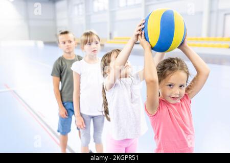 Mädchen, die den Ball an eine Freundin weitergibt, die sich am Schulsportplatz anstellt Stockfoto