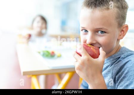 Schuljunge isst frischen Apfel in der Mittagspause in der Cafeteria Stockfoto