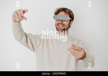 Lächelnder Ingenieur mit VR-Brille, der vor der weißen Wand Gesten trägt Stockfoto