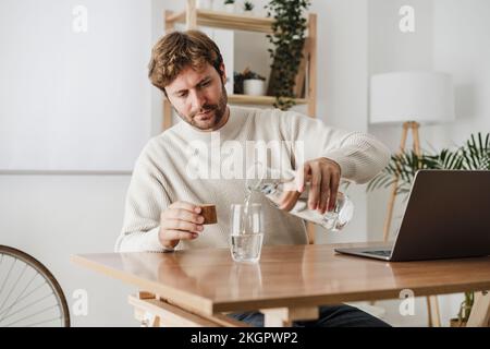Geschäftsmann, der im Büro Wasser aus der Flasche in Glas gießt Stockfoto