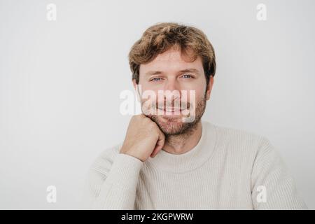 Lächelnder, gutaussehender Geschäftsmann mit Hand am Kinn vor der weißen Wand Stockfoto
