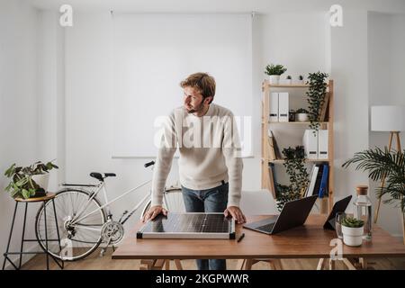 Vorausschauender Geschäftsmann mit Solarmodul auf dem Schreibtisch am Arbeitsplatz Stockfoto