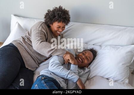 Mutter kitzelnder Sohn, der zu Hause im Bett liegt Stockfoto