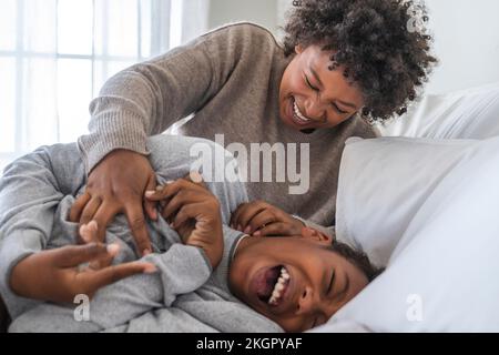 Glückliche Mutter kitzeln Junge auf Bett zu Hause Stockfoto