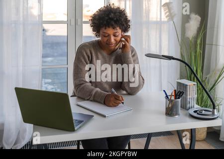 Freiberufler, der über ein Smartphone spricht und sich zu Hause Notizen macht Stockfoto