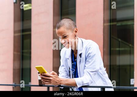 Lächelnder reifer Arzt mit Handy ausserhalb des Krankenhauses Stockfoto