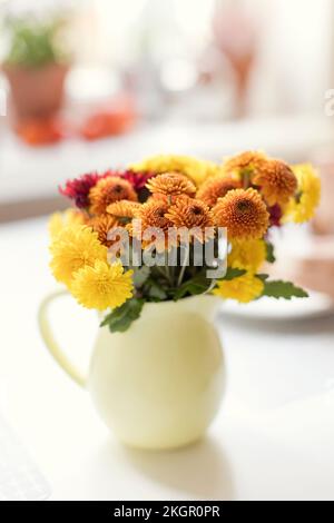 Gelbe und orangefarbene Chrysanthemblüten im Krug auf dem Tisch Stockfoto