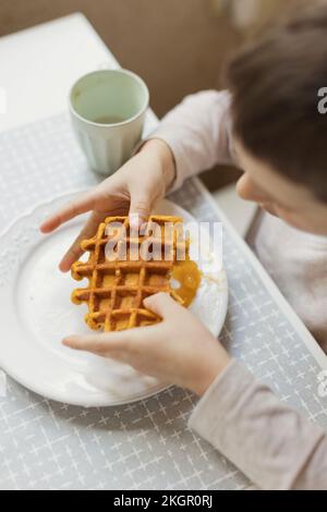 Ein Junge, der Waffel auf dem Esstisch in der Küche hält Stockfoto
