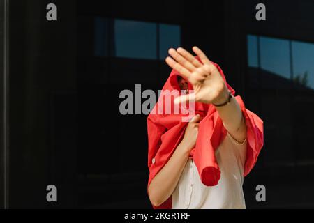 Geschäftsfrau mit rotem Blazer und Gestenstopp-Schild an sonnigen Tagen Stockfoto