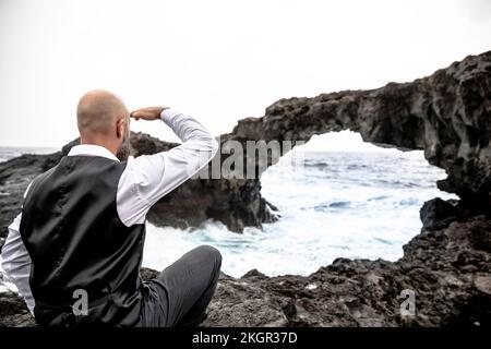 Reifer Mann schützt Augen vor dem Felsbogen Stockfoto