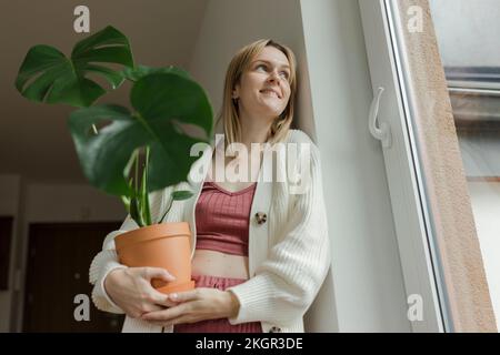 Denkwürdige Frau, die zu Hause Monstera-Pflanzen an der Wand hält Stockfoto