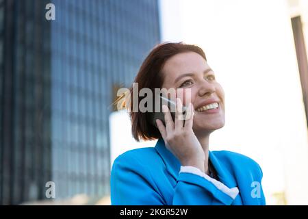 Glückliche Geschäftsfrau, die über ihr Smartphone nachdenkt und spricht Stockfoto