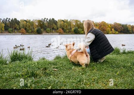 Eine Frau und ein Hund auf Gras, die Enten im See beobachten Stockfoto