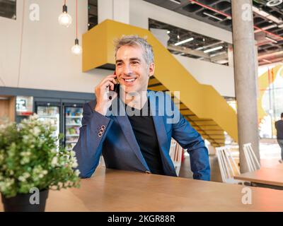 Glücklicher, reifer Geschäftsmann, der in der Cafeteria telefoniert Stockfoto