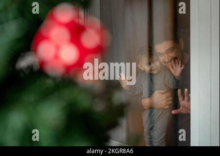 Vater und Sohn schauen zu Hause aus dem Fenster auf den Weihnachtsbaum Stockfoto