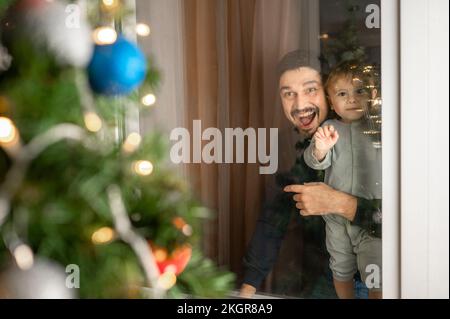 Glücklicher Vater mit Sohn, der den Weihnachtsbaum durchs Fenster sieht Stockfoto