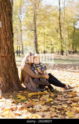 Süßer Junge, der im Park auf dem Schoß seiner Mutter sitzt Stockfoto