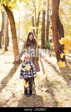 Mutter wirft Herbstblätter über den Sohn im Park Stockfoto
