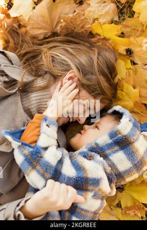 Mutter und Sohn liegen auf gelben Herbstblättern im Park Stockfoto