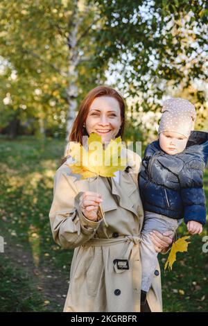 Glückliche Frau mit Ahornblatt tragender Tochter Stockfoto