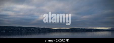 Ein Panoramablick auf einen See unter einem wolkigen stürmischen Himmel mit Land in der Ferne Stockfoto