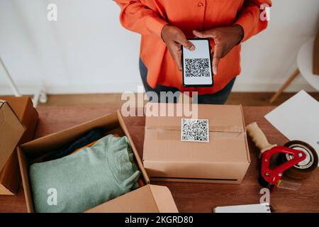 Eine Geschäftsfrau scannt den QR-Code auf dem Paket an der Rezeption Stockfoto