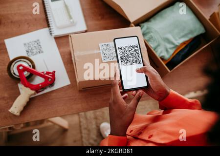 Hände einer Geschäftsfrau, die den QR-Code über ein Smartphone scannt, auf der Verpackung am Schreibtisch Stockfoto