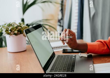 Hand eines Freiberuflers, der auf den Laptop-Bildschirm zeigt, mit Stift am Schreibtisch Stockfoto