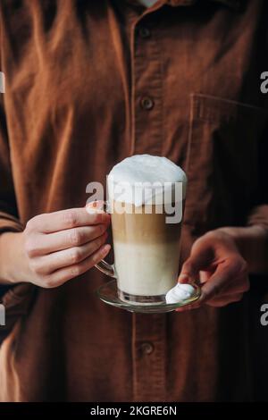 Hände einer Frau, die ein Glas Cappuccino hält Stockfoto