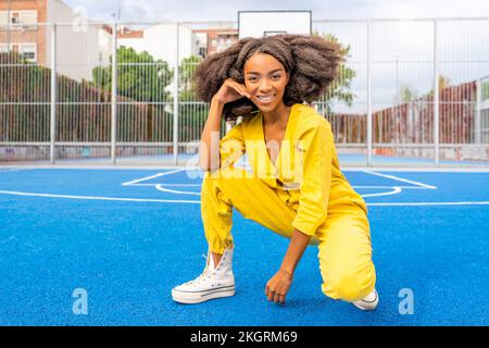 Lächelnde Frau, die das Gesicht berührt und sich auf dem Basketballfeld duckt Stockfoto